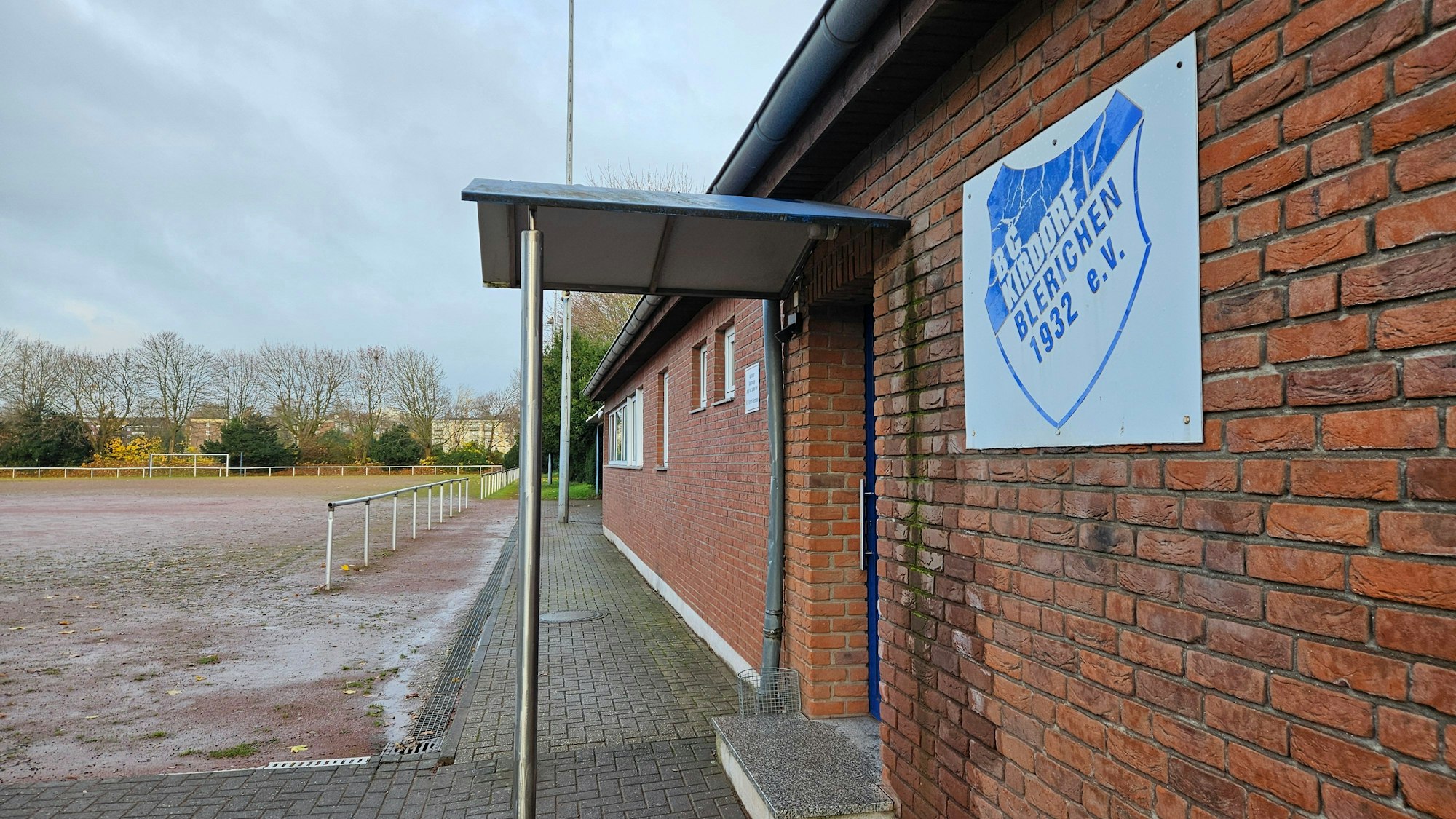 Ein eingeschossiges Backsteingebäude steht neben einem Tennenplatz.