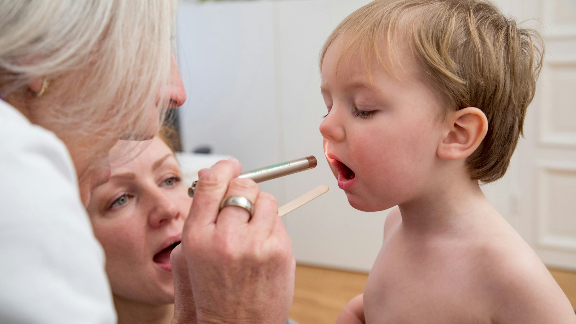 Eine Ärztin leuchtet einem kleinen Jungen in den Rachen.