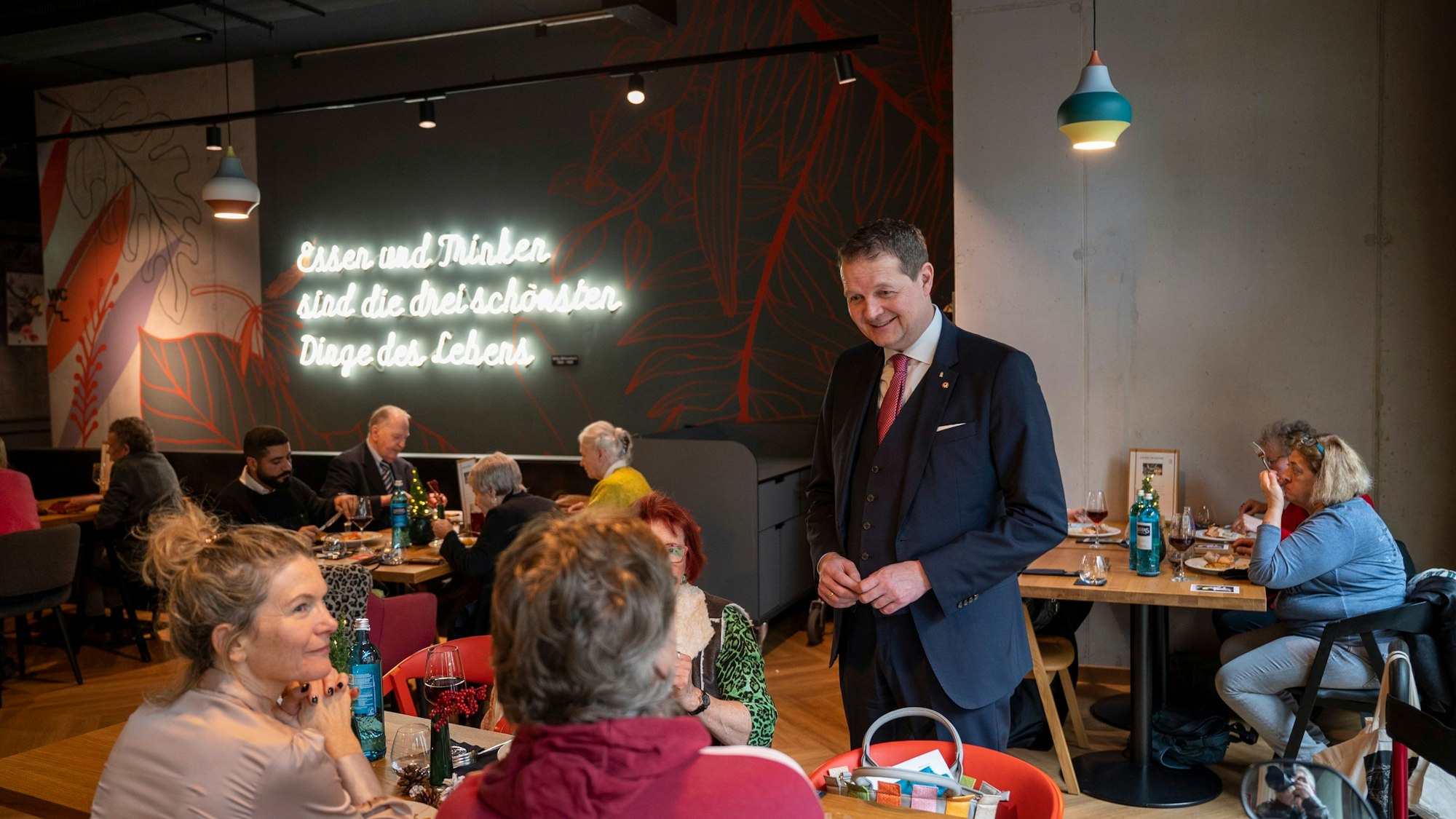 Boris Müller lächelt und schaut Senioren an, die an Bänken sitzen.