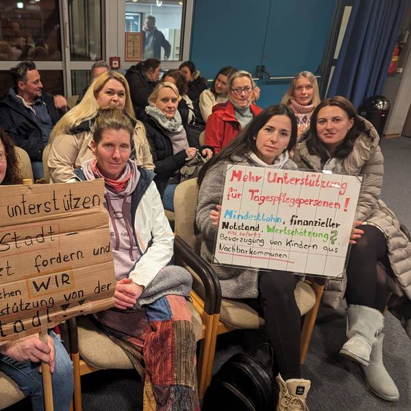 Eine Gruppe von Frauen mit zwei Protestplakaten auf den Zuschauerplätzen im Deutschordensaal des Bürgerhauses.