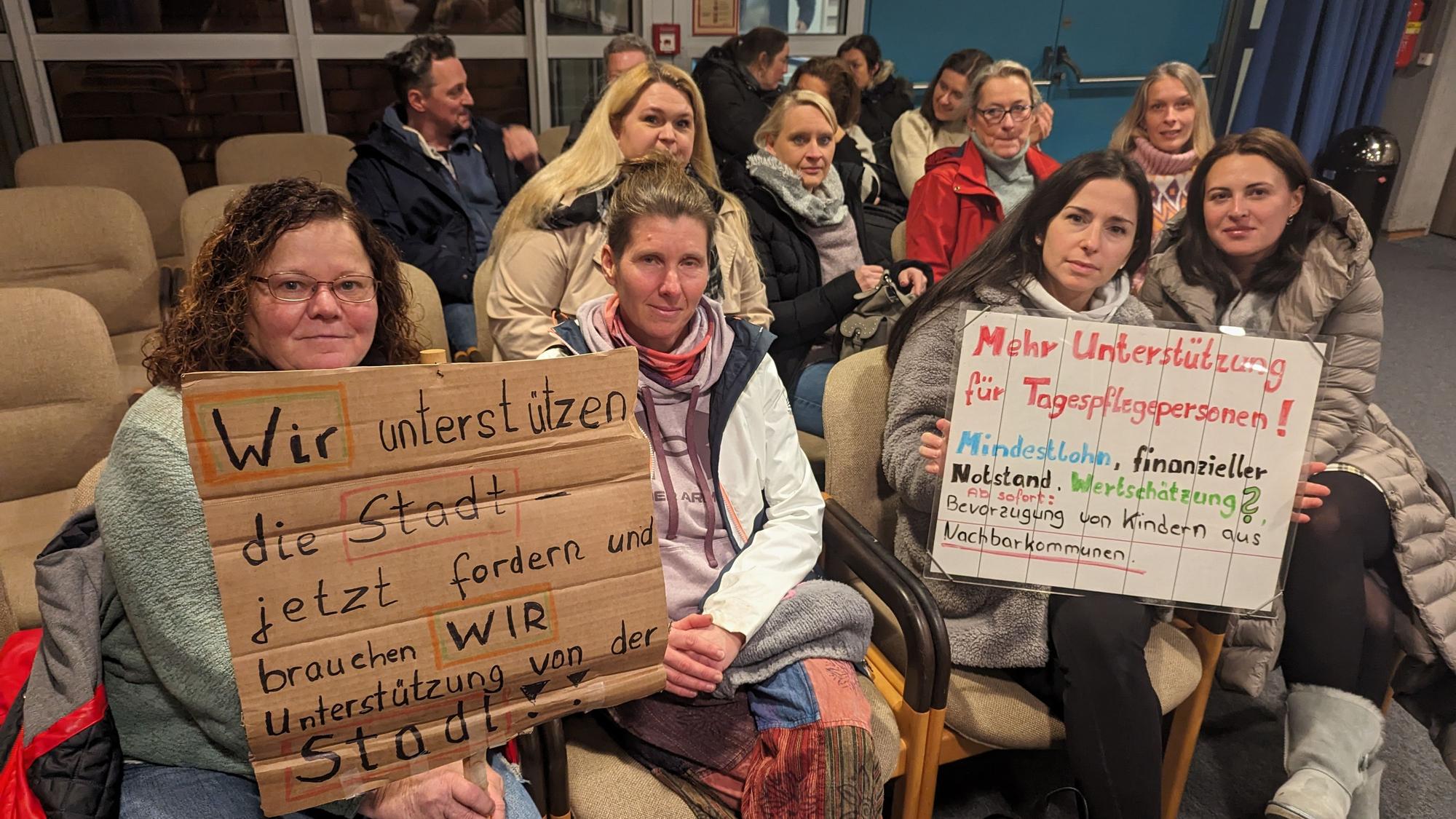Eine Gruppe von Frauen mit zwei Protestplakaten auf den Zuschauerplätzen im Deutschordensaal des Bürgerhauses.