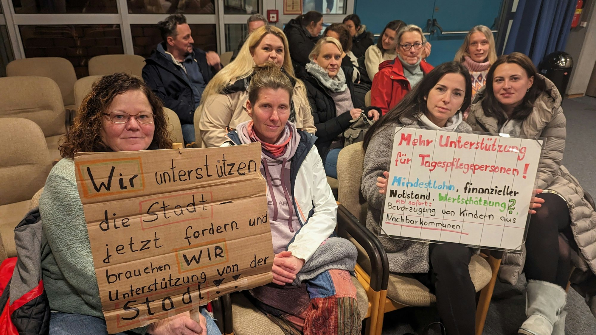 Eine Gruppe von Frauen mit zwei Protestplakaten auf den Zuschauerplätzen im Deutschordensaal des Bürgerhauses.