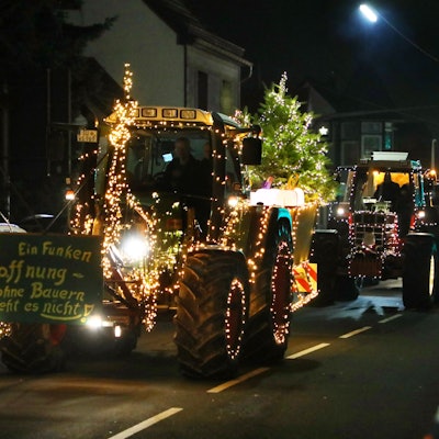 Mit Lichterketten verzierten Traktoren fahren in einer Kolonne über eine Straße.