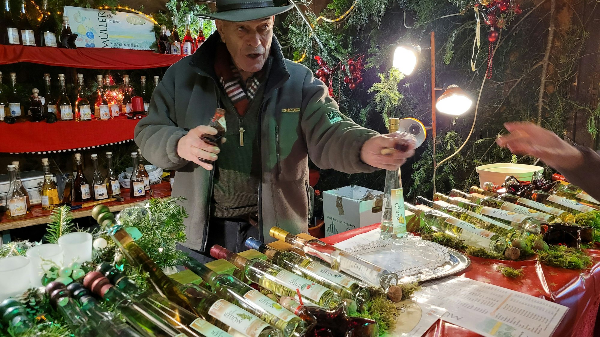 Ein Mann bietet eine Likörprobe an. Sein Stand ist gefüllt mit Flaschen.