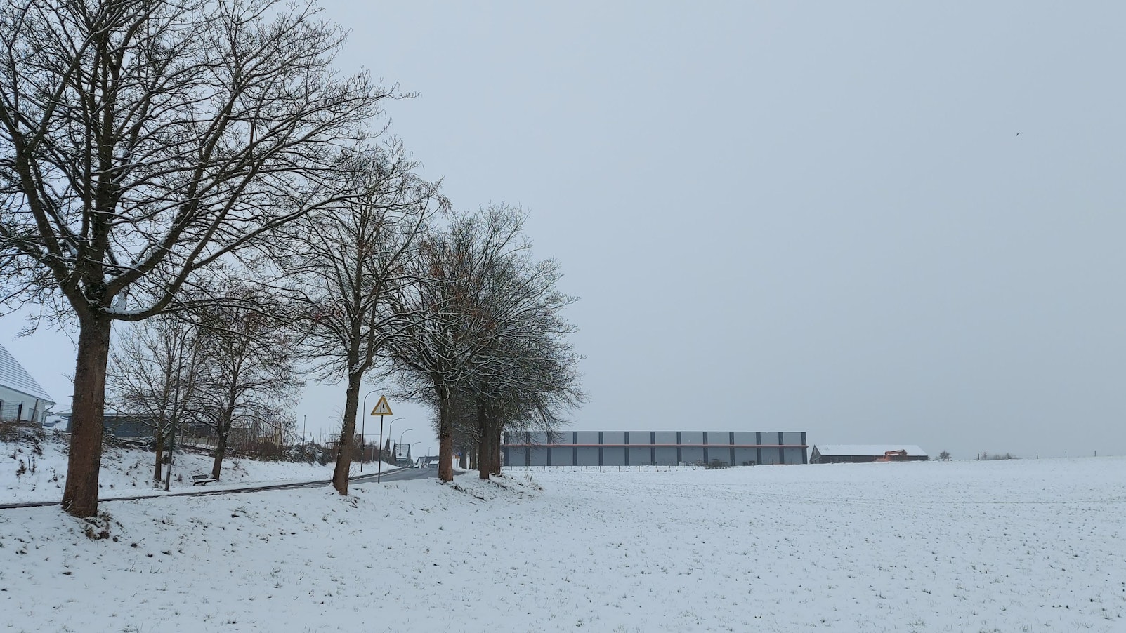 Gezeigt wird ein verschneiter Acker, am linken Bildrand befinden sich Häuser.