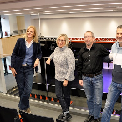 Zwei Frauen und zwei Männer stehen auf der Empore einer Aula.