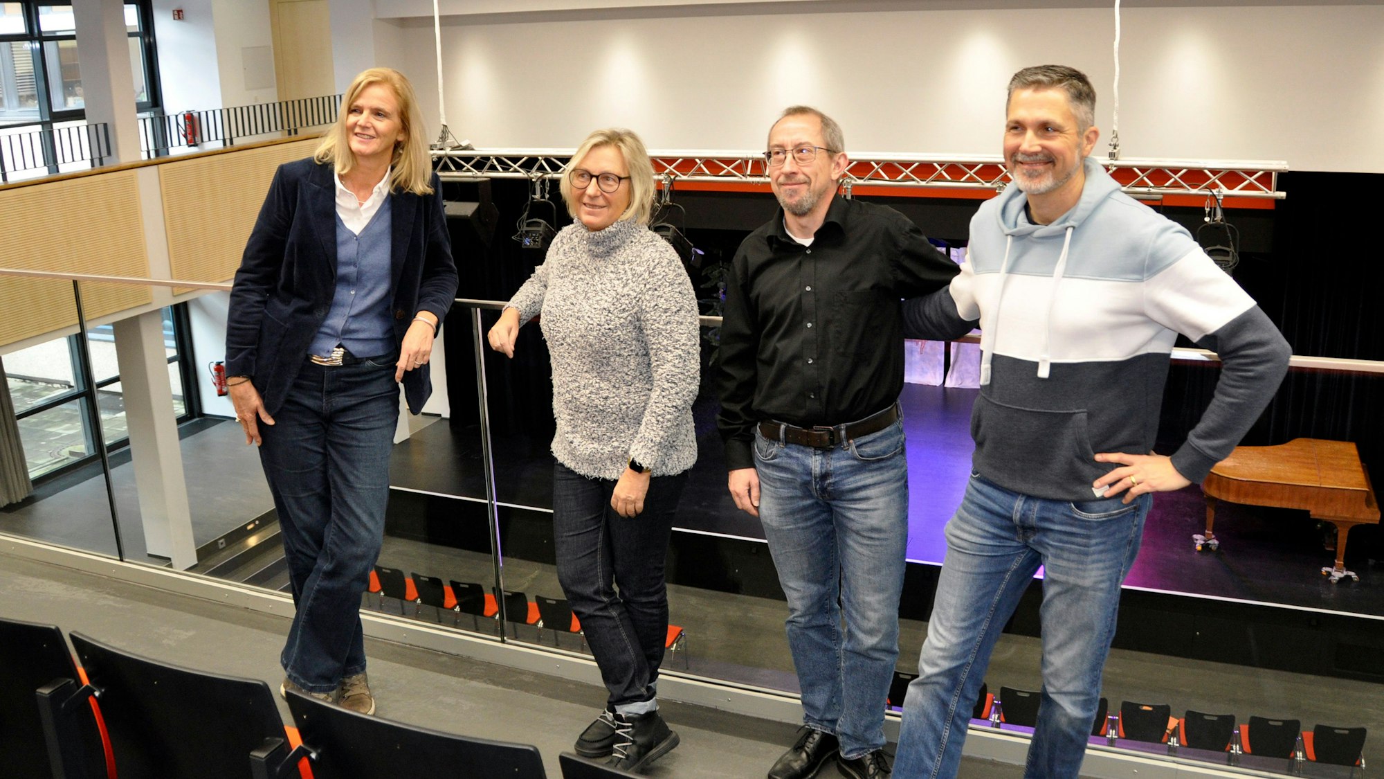 Zwei Frauen und zwei Männer stehen auf der Empore einer Aula.