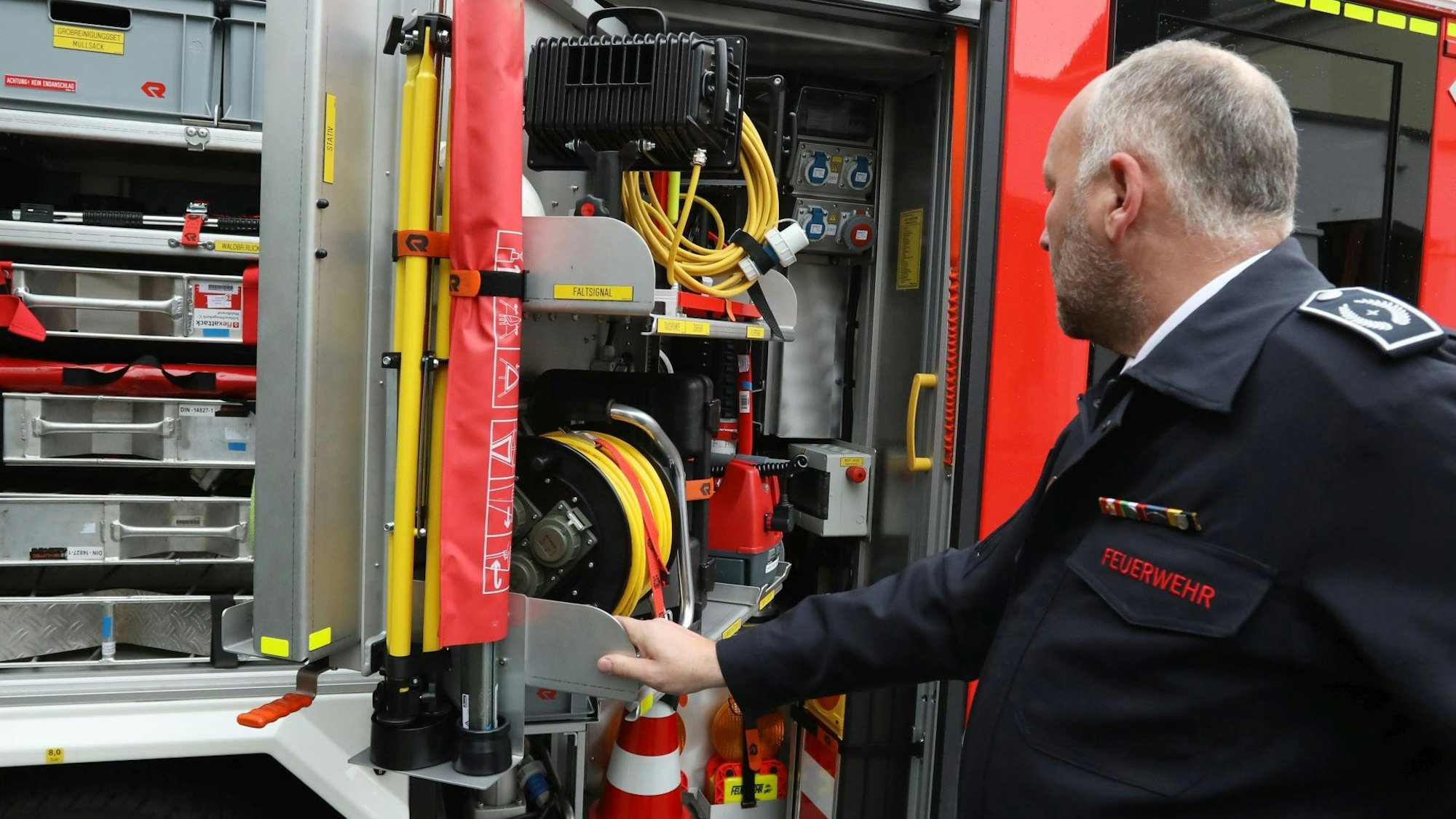 Ein Feuerwehrmann steht an einer geöffneten Klappe des neuen Löschfahrzeugs und zeigt dessen Ausstattung.
