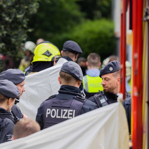 Eine Person wird vor einem Hochhaus, abgeschirmt von Feuerwehr und Polizei, in einen Krankenwagen gebracht.