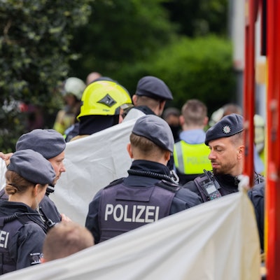 Eine Person wird vor einem Hochhaus, abgeschirmt von Feuerwehr und Polizei, in einen Krankenwagen gebracht.