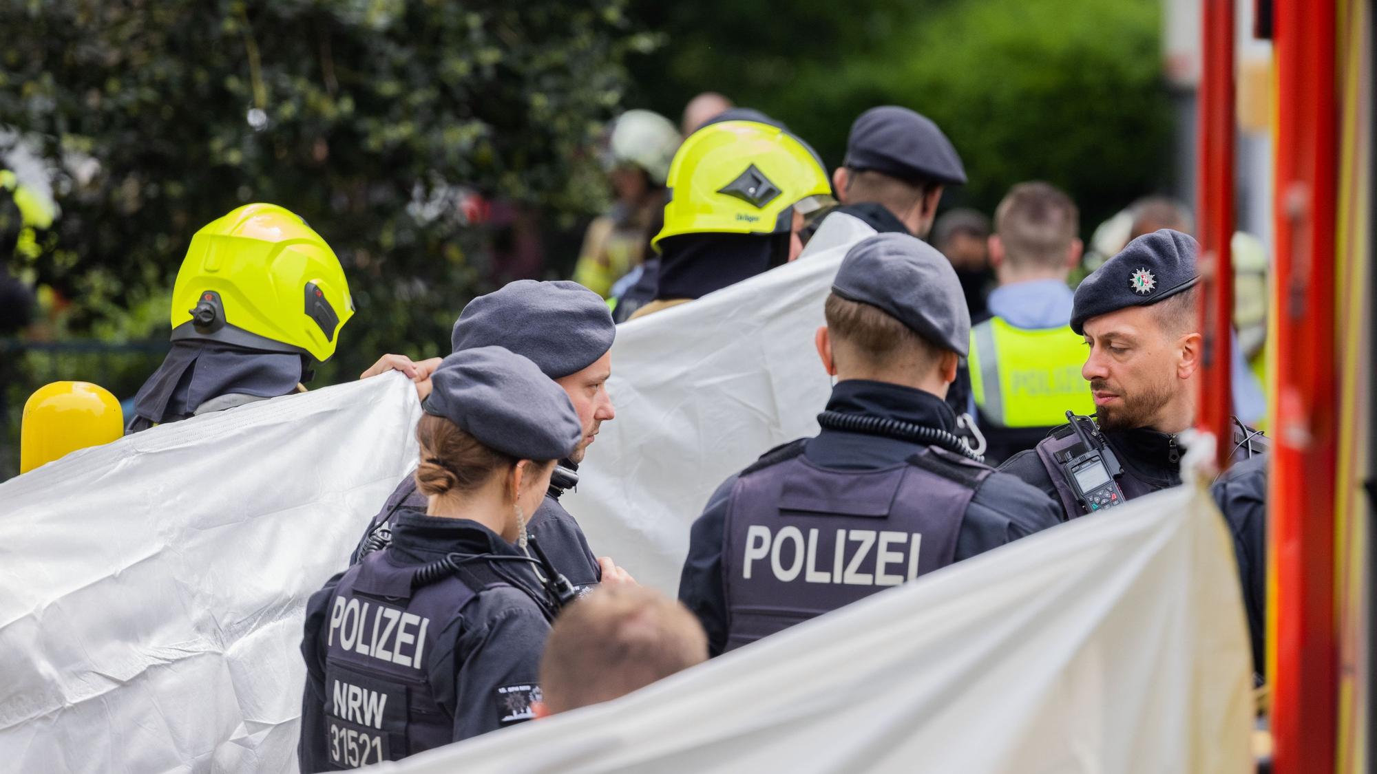 Eine Person wird vor einem Hochhaus, abgeschirmt von Feuerwehr und Polizei, in einen Krankenwagen gebracht.