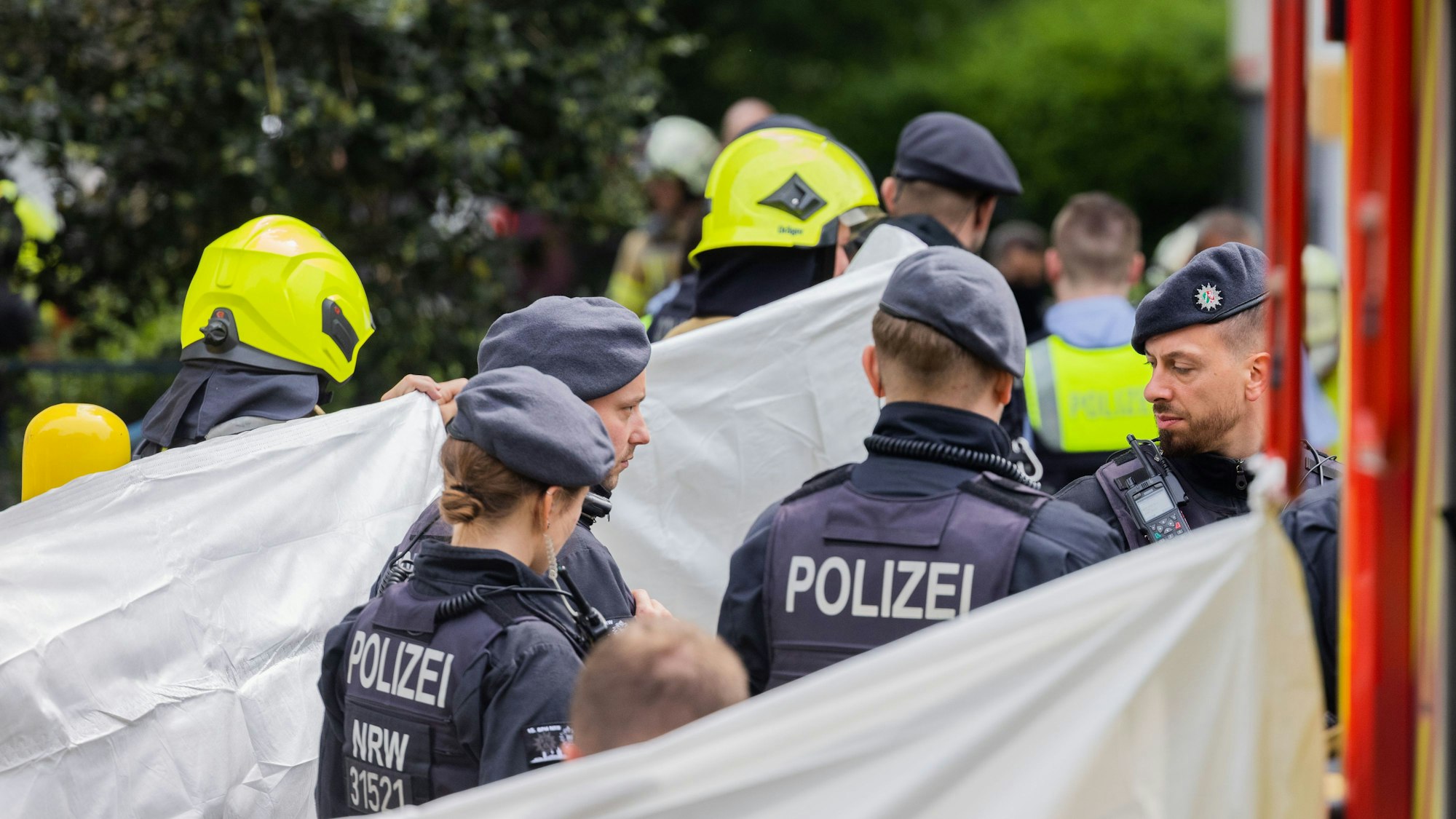Eine Person wird vor einem Hochhaus, abgeschirmt von Feuerwehr und Polizei, in einen Krankenwagen gebracht.