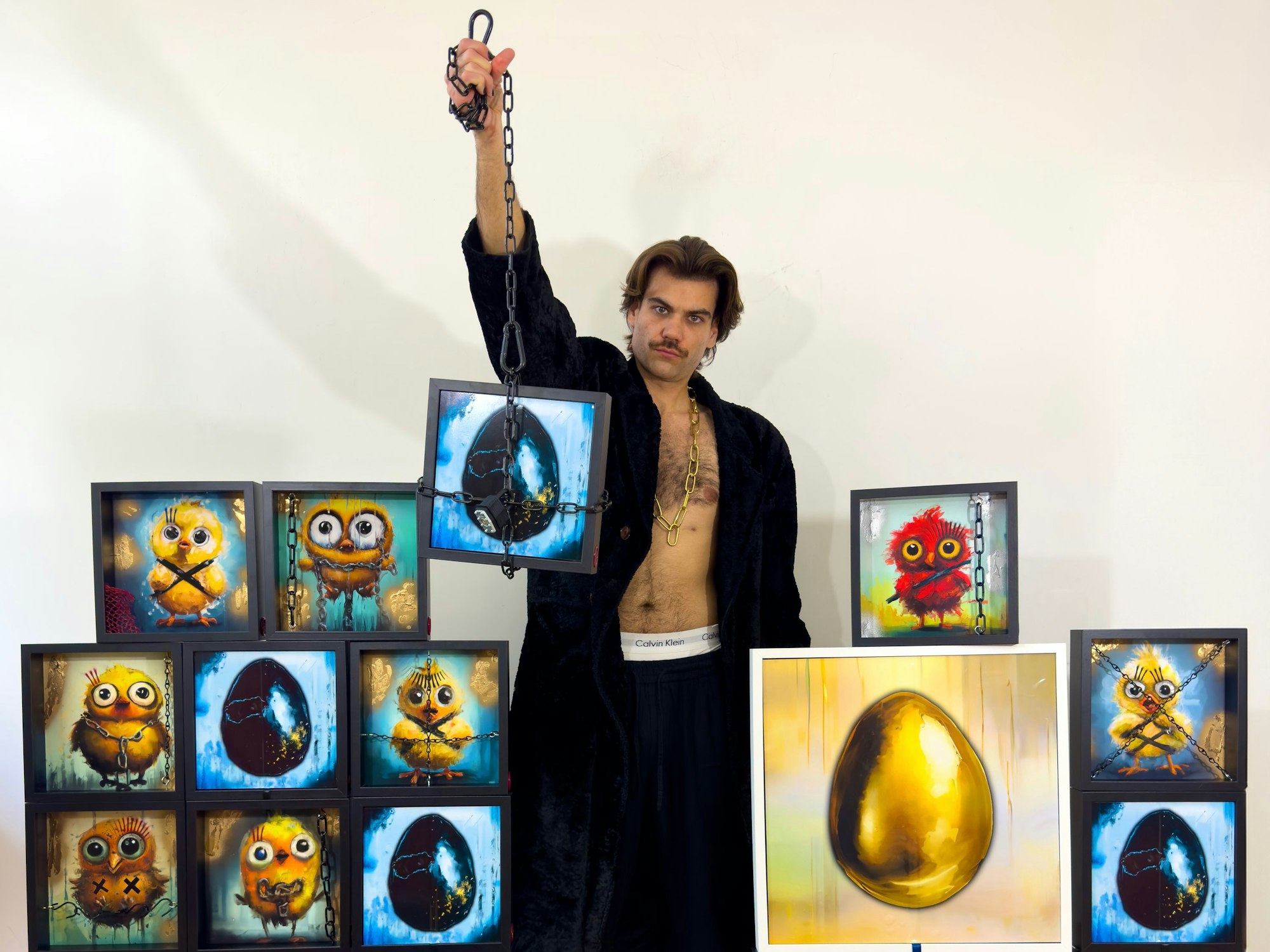 Leinfelder steht zwischen seinen Bildern und hält eines hoch