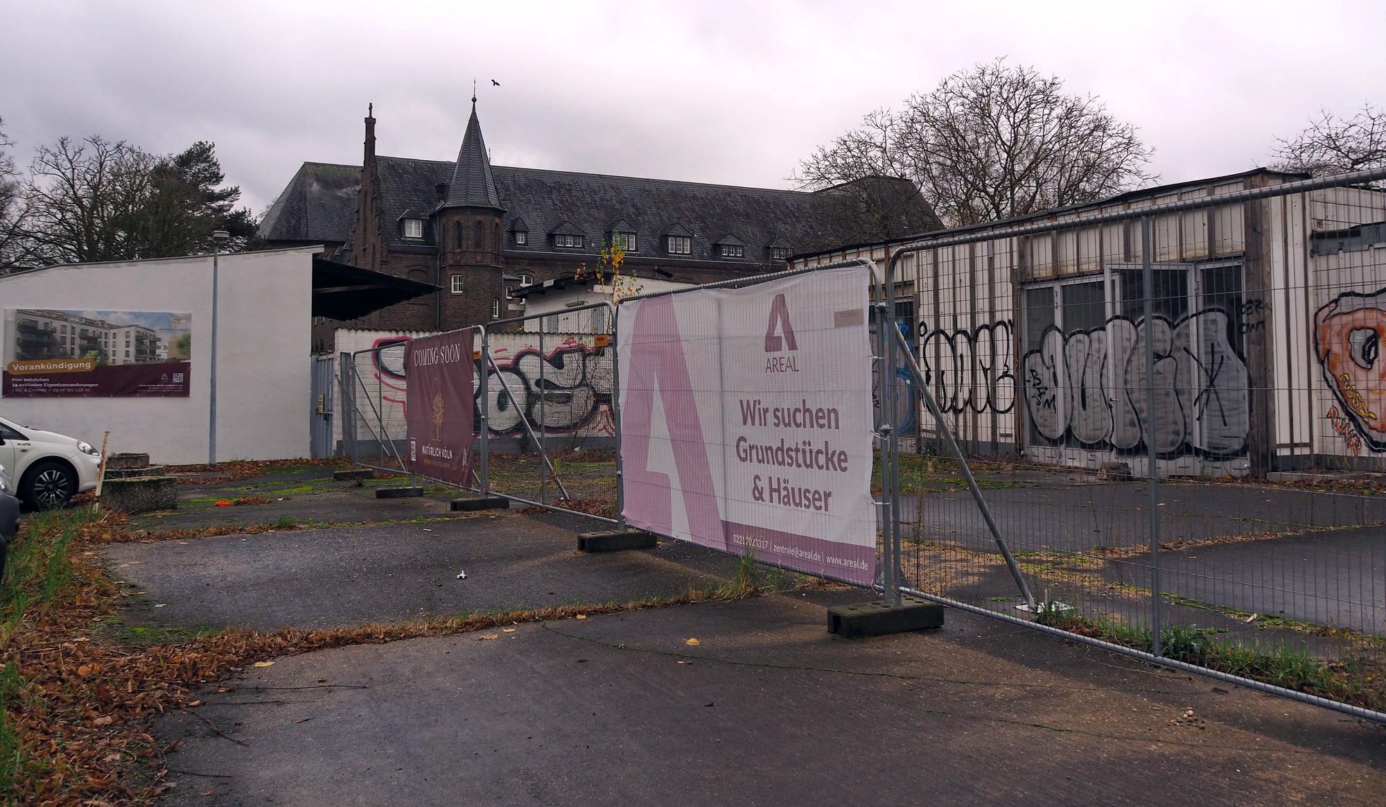 Das Grundstück an der Brühler Straße hinter einem Bauzaun. Im Hintergrund ist das Kloster der Benediktinerinnen zu sehen.