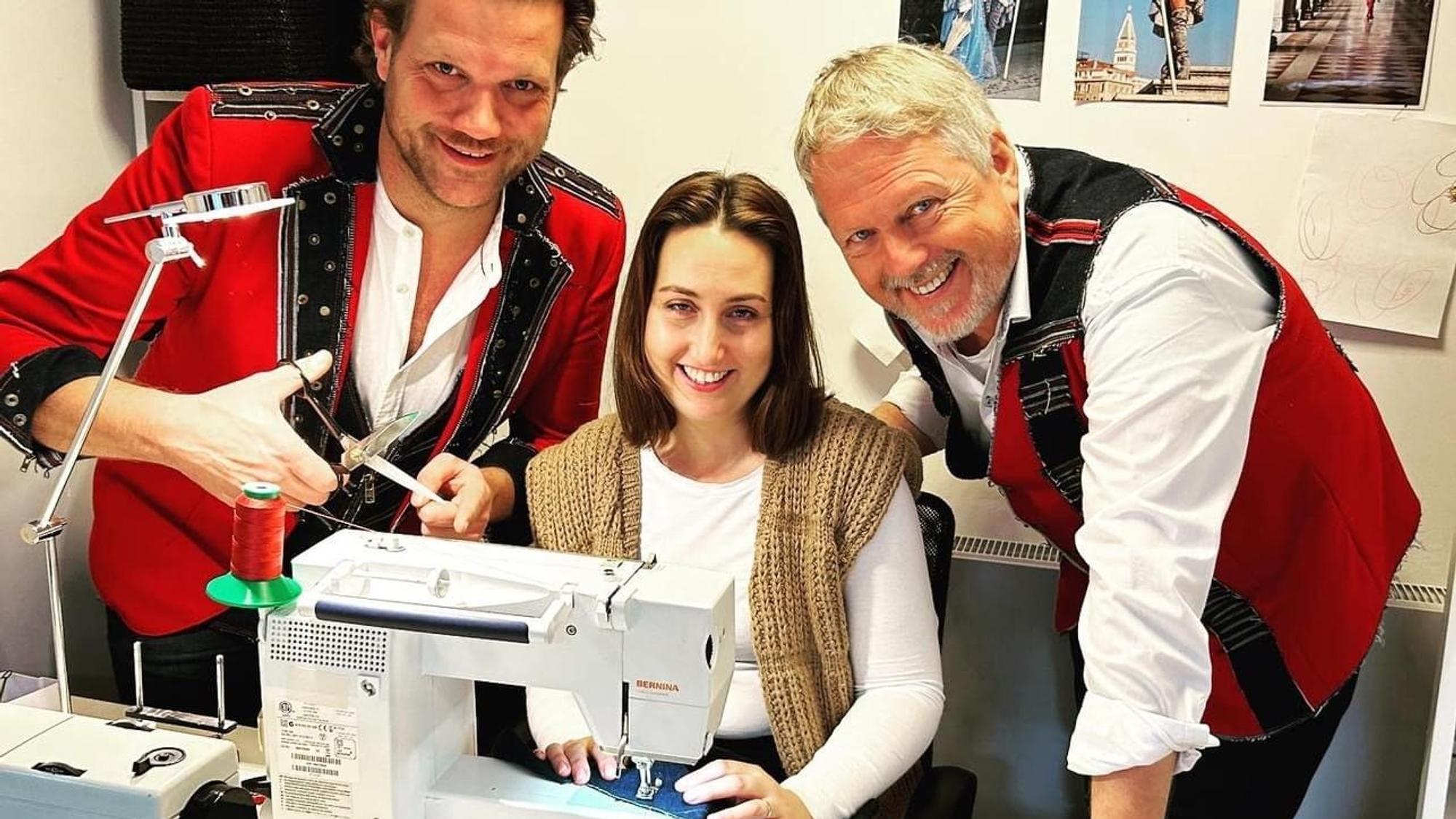 Alex Barth und Benjamin Weissert stehen neben Jasmin Engel, die an einer Nähmaschine sitzt.