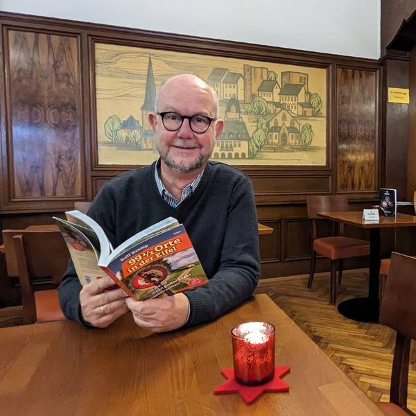 Autor und Verleger Ralf Kramp sitzt mit einem aufgeschlagenen Buch im Café Kramer in Euskirchen.