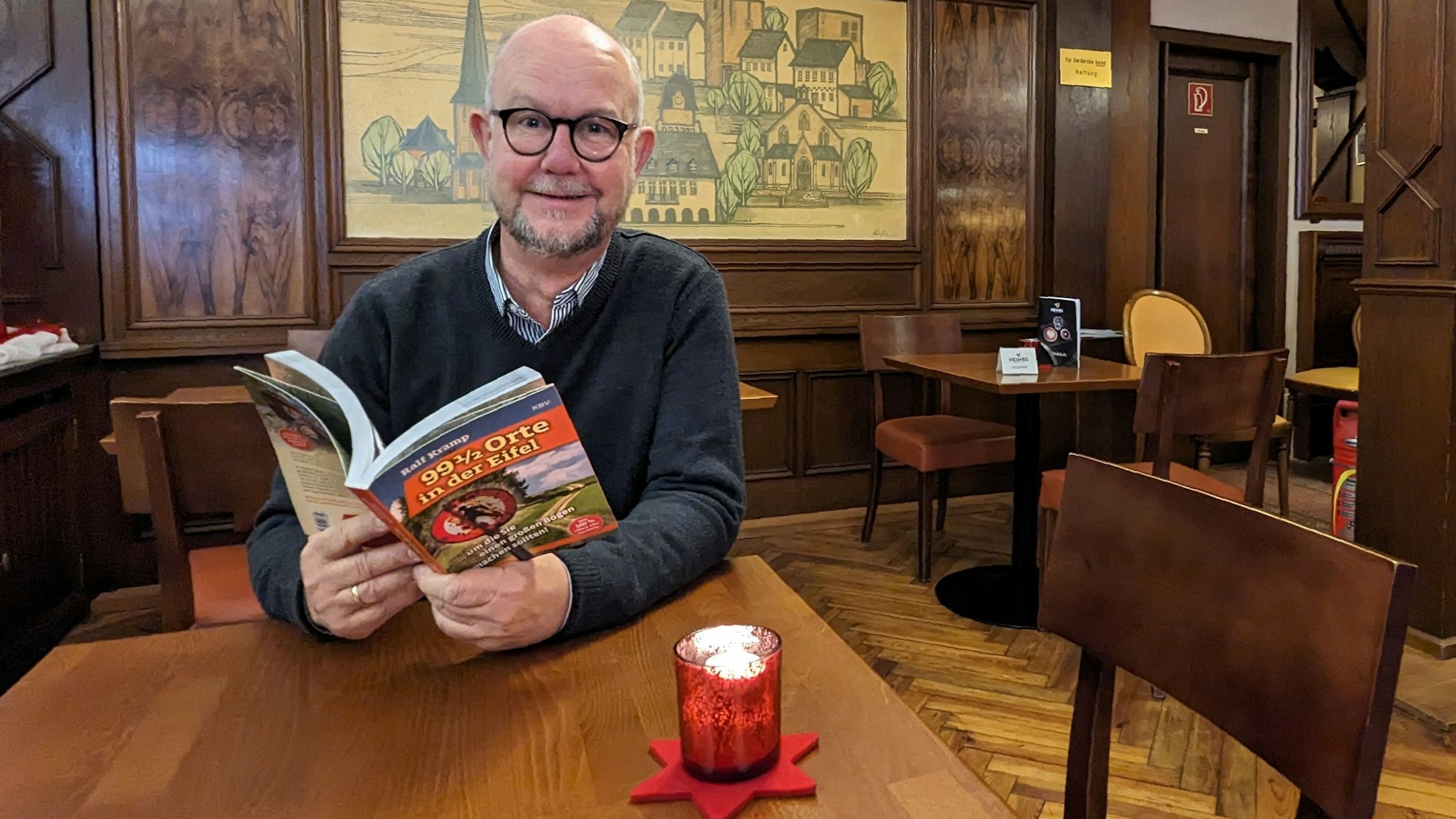Ralf Kramp sitzt mit seinem neuen Buch an einem Tisch im Café Kramer in Euskirchen.