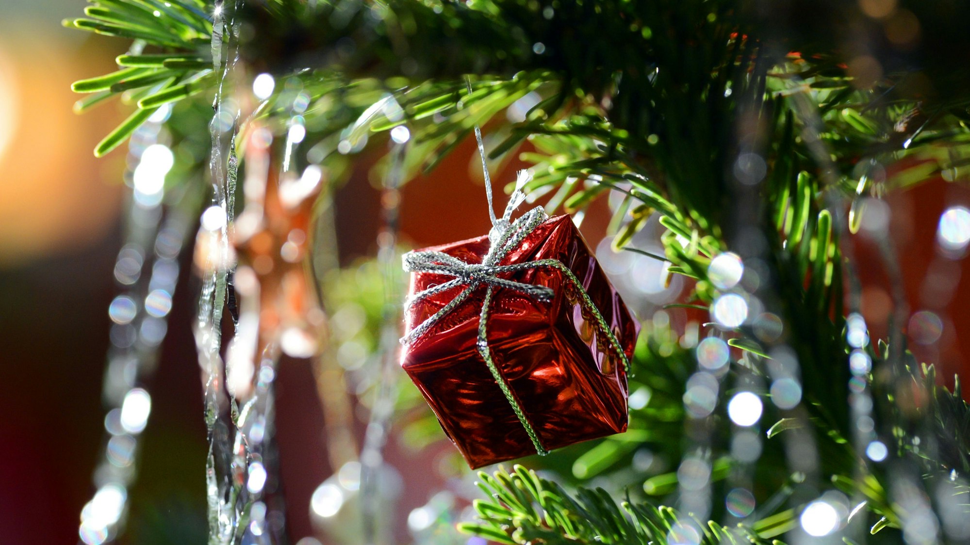 Ein kleines rotes Geschenkpaket als Weihnachtsbaumanhänger und Lametta hängen am 30.12.2012 an einem Weihnachtsbaum.