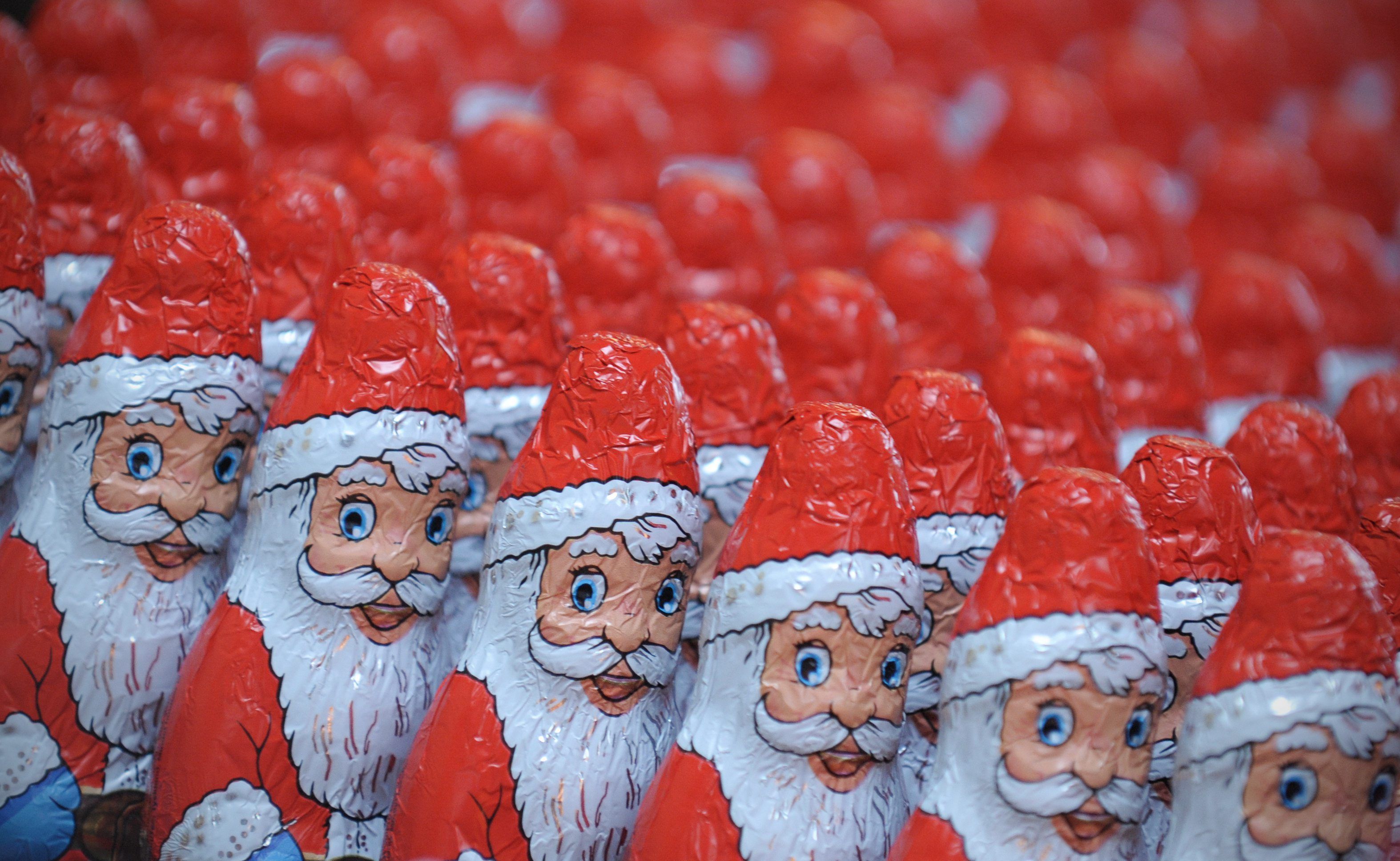 Viele Schokoladen Weihnachtsmänner stehen aufgereiht neben- und hintereinander.