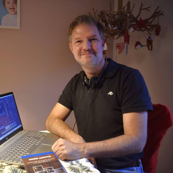 Stephan Gatzweiler sitzt an einem adventlich dekorierten Tisch, vor ihm steht ein Laptop, auf dem ein offenes Schnittprogramm zu sehen ist.