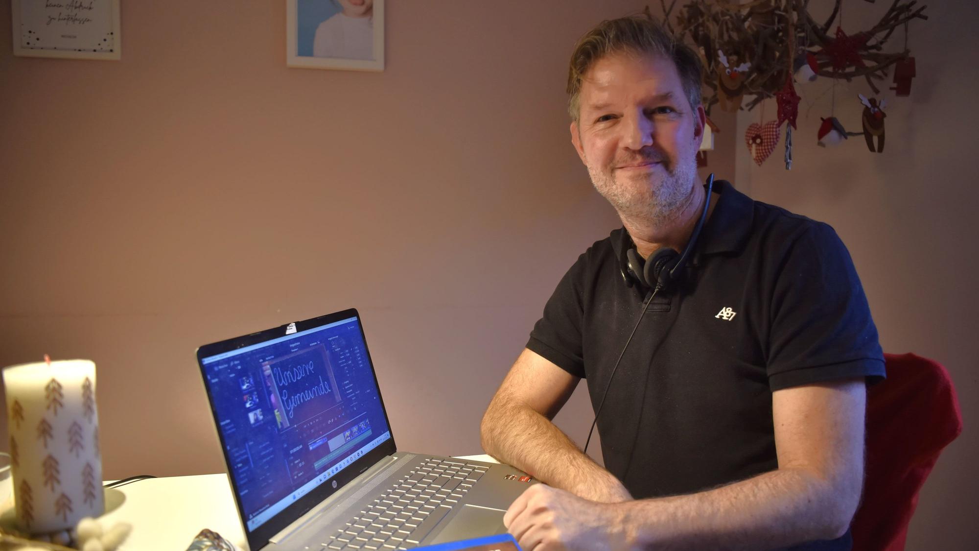 Stephan Gatzweiler sitzt an einem adventlich dekorierten Tisch, vor ihm steht ein Laptop, auf dem ein offenes Schnittprogramm zu sehen ist.