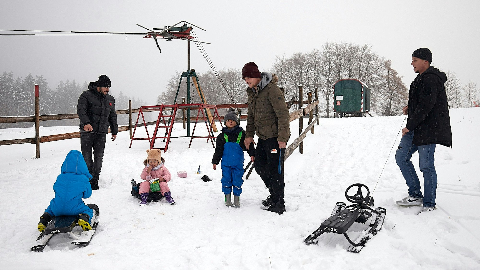 Drei Männer und drei Kinder haben in Udenbreth Spaß auf ihren Schlitten im Schnee.