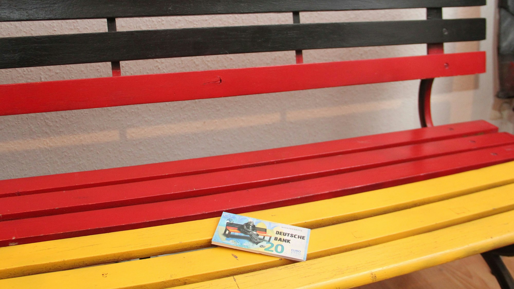 Der von Künstler Peter Mück erschaffene 20-Euro-Schein liegt auf einer schwarz-rot-golden lackierten Bank.