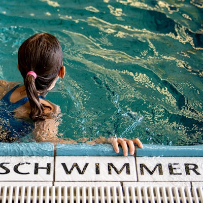 Ein Kind schwimmt in einem Schwimmbad. Auf den Fliesen steht die Aufschrift „Nur für Schwimmer“.