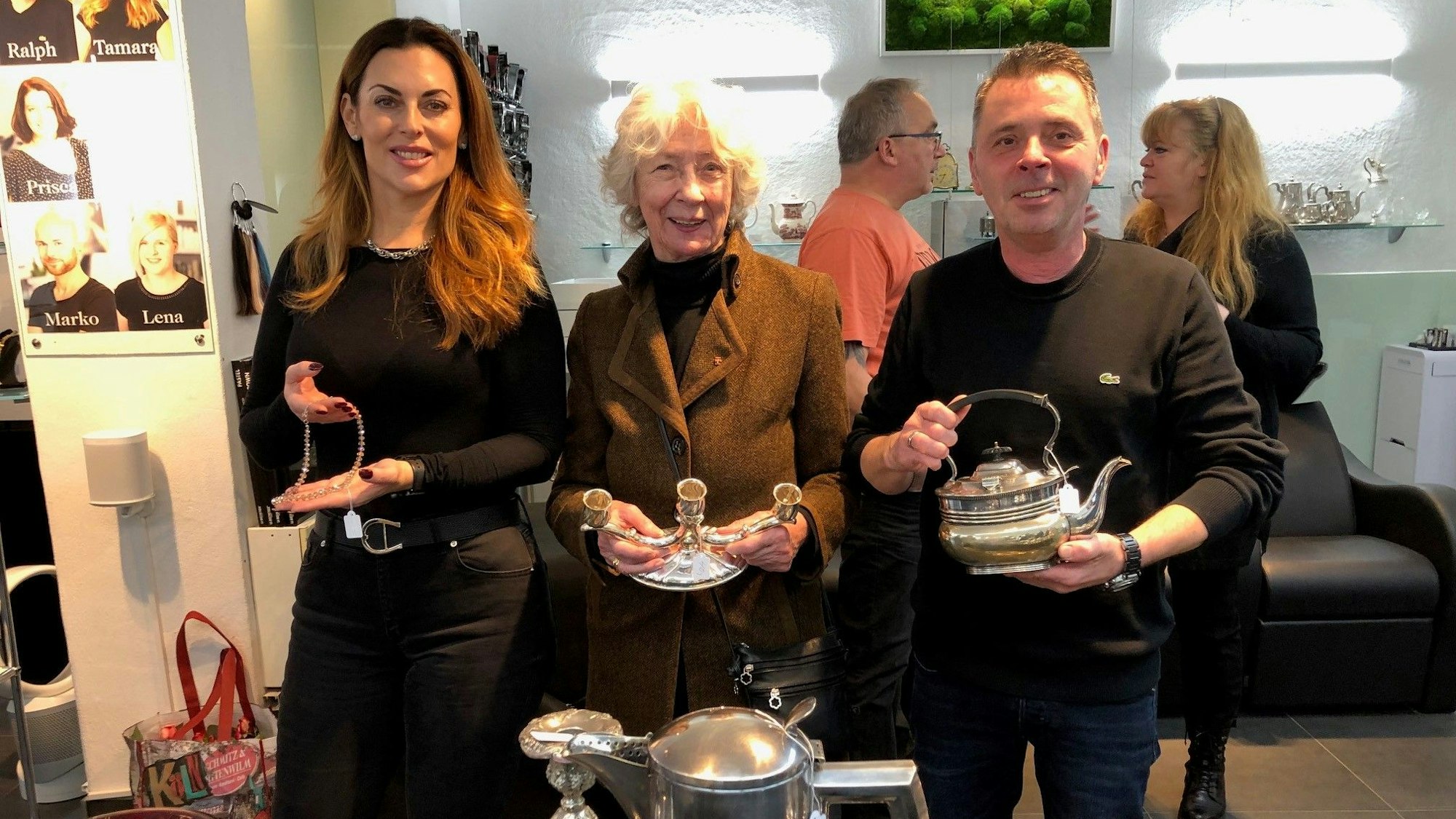 Salon-Mitarbeiterin Tamara Ergiden, Hedwig Neven DuMont und Ralph Schwalbach halten bei der Eröffnung der Benefiz-Börse„ Schmuckstücke im Salon“ kostbares Silber in der Hand.