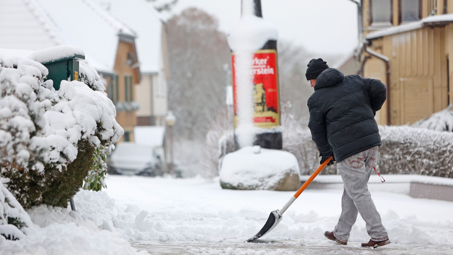 Ein Mann schiebt Schnee vom Gehweg.