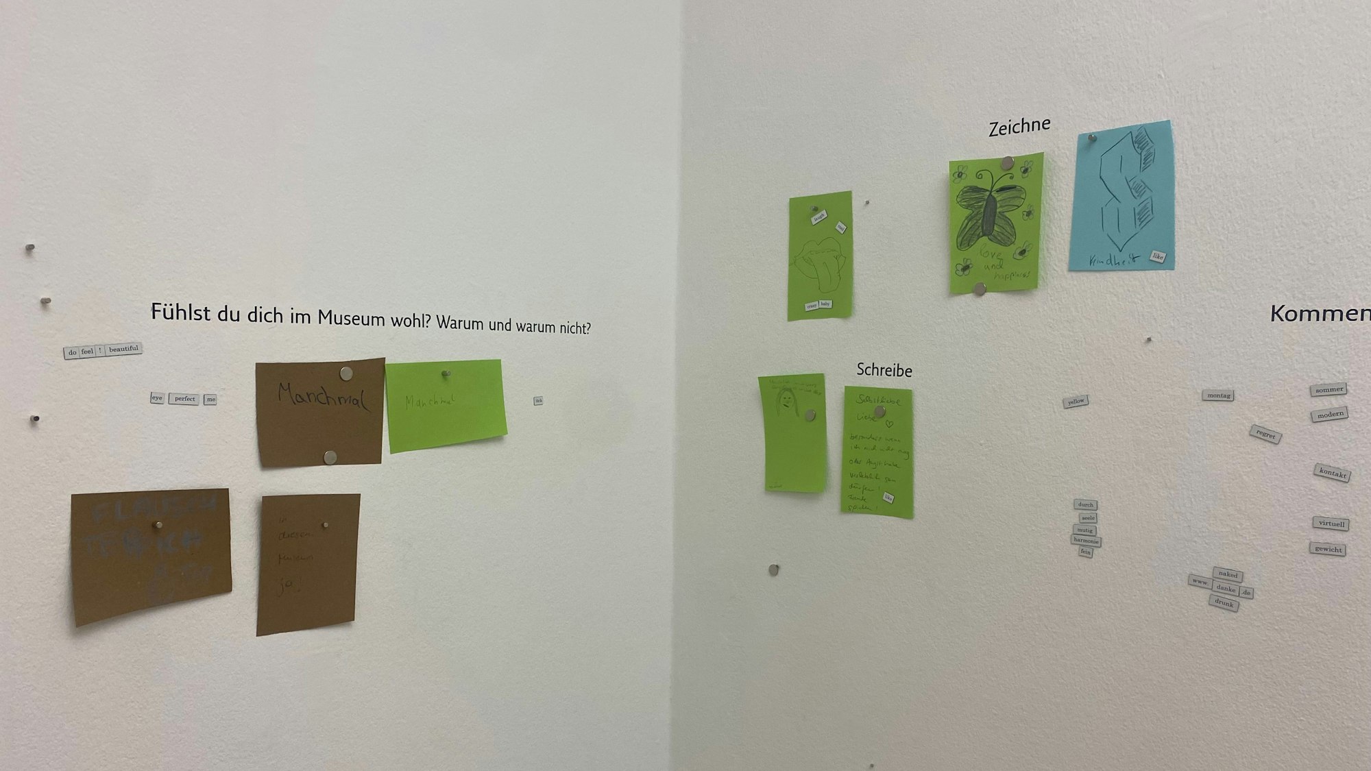 An einer weißen Wand hängen Zeichnungen und Zettel.