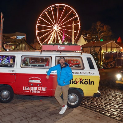 Roman Bendt steht vor dem roten VW-Bulli, hinter ihm das Riesenrad und die Hütten des Hafen-Weihnachtsmarkts.