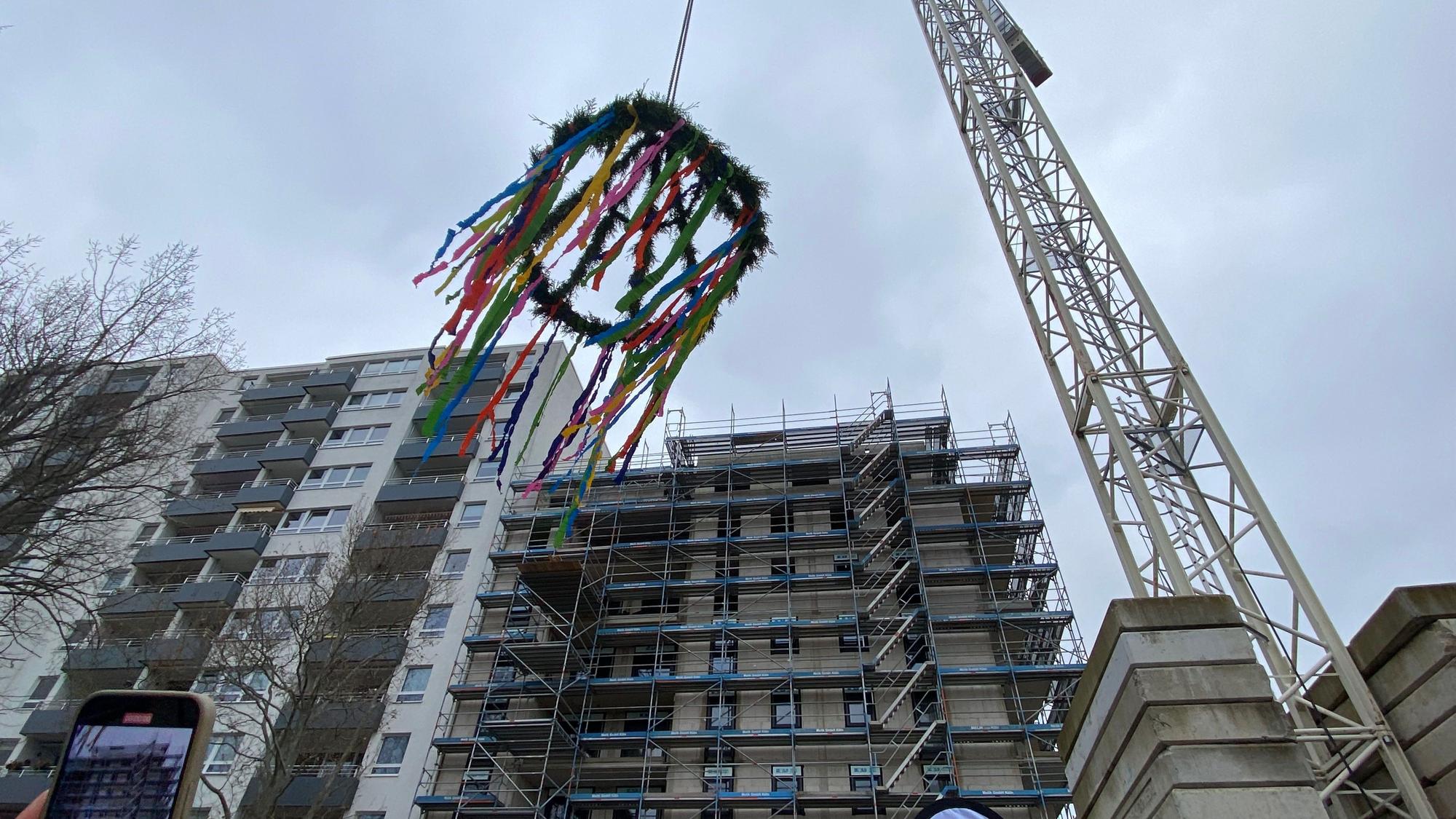 Der Richtkranz hängt an einem Kran, im Hintergrund ist der achtstöckige Neubau zu sehen.