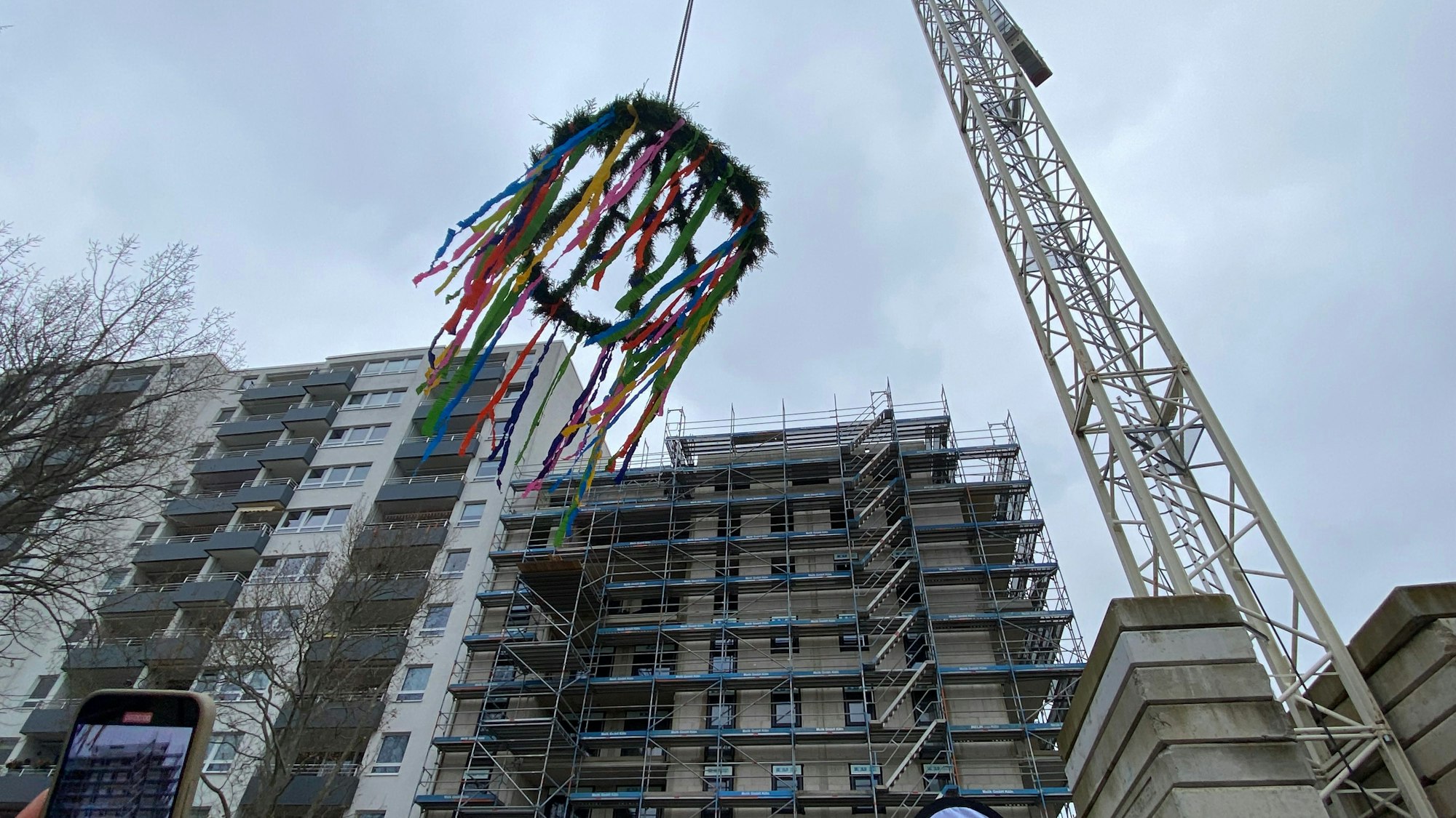 Der Richtkranz hängt an einem Kran, im Hintergrund ist der achtstöckige Neubau zu sehen.