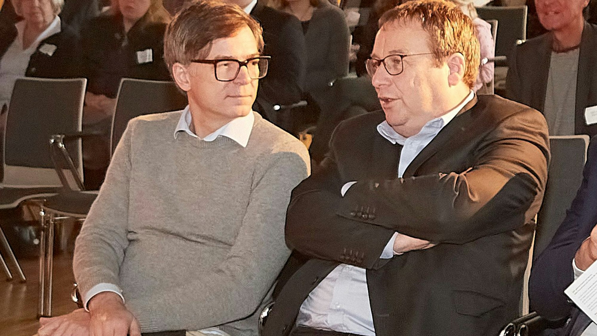 Ralph Caspers und Oliver Krischer sitzen unter den Gästen und unterhalten sich.