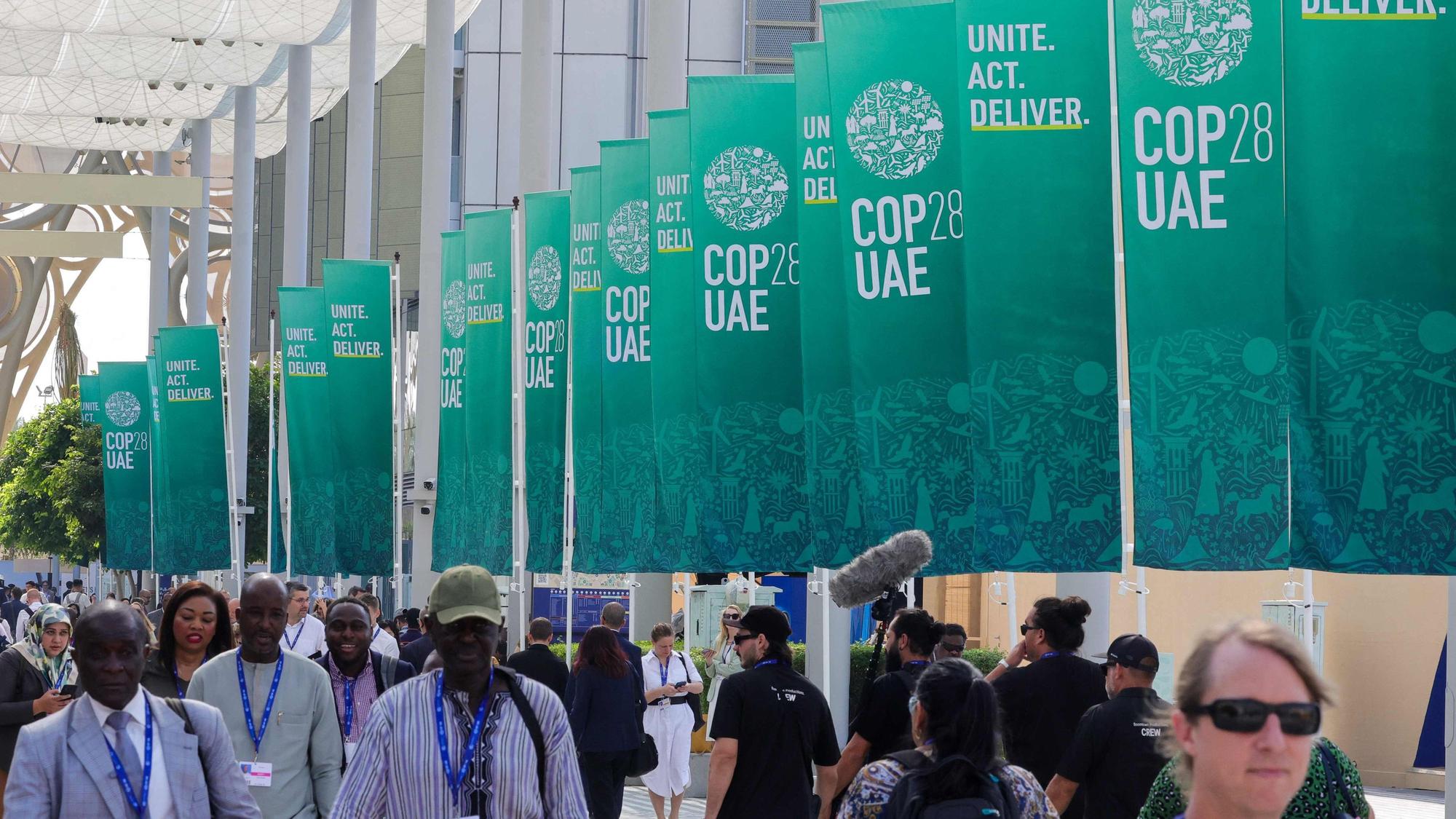 Participants walk past banners at the COP28 United Nations climate summit in Dubai on December 3, 2023. (Photo by Giuseppe CACACE / AFP)