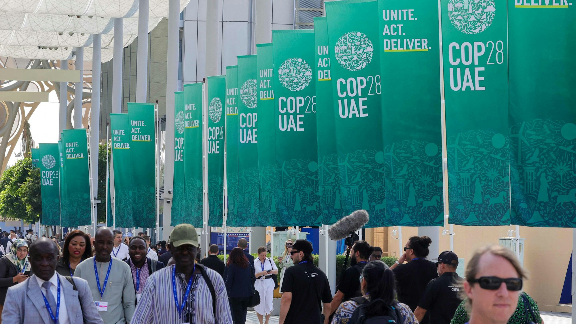 Participants walk past banners at the COP28 United Nations climate summit in Dubai on December 3, 2023. (Photo by Giuseppe CACACE / AFP)