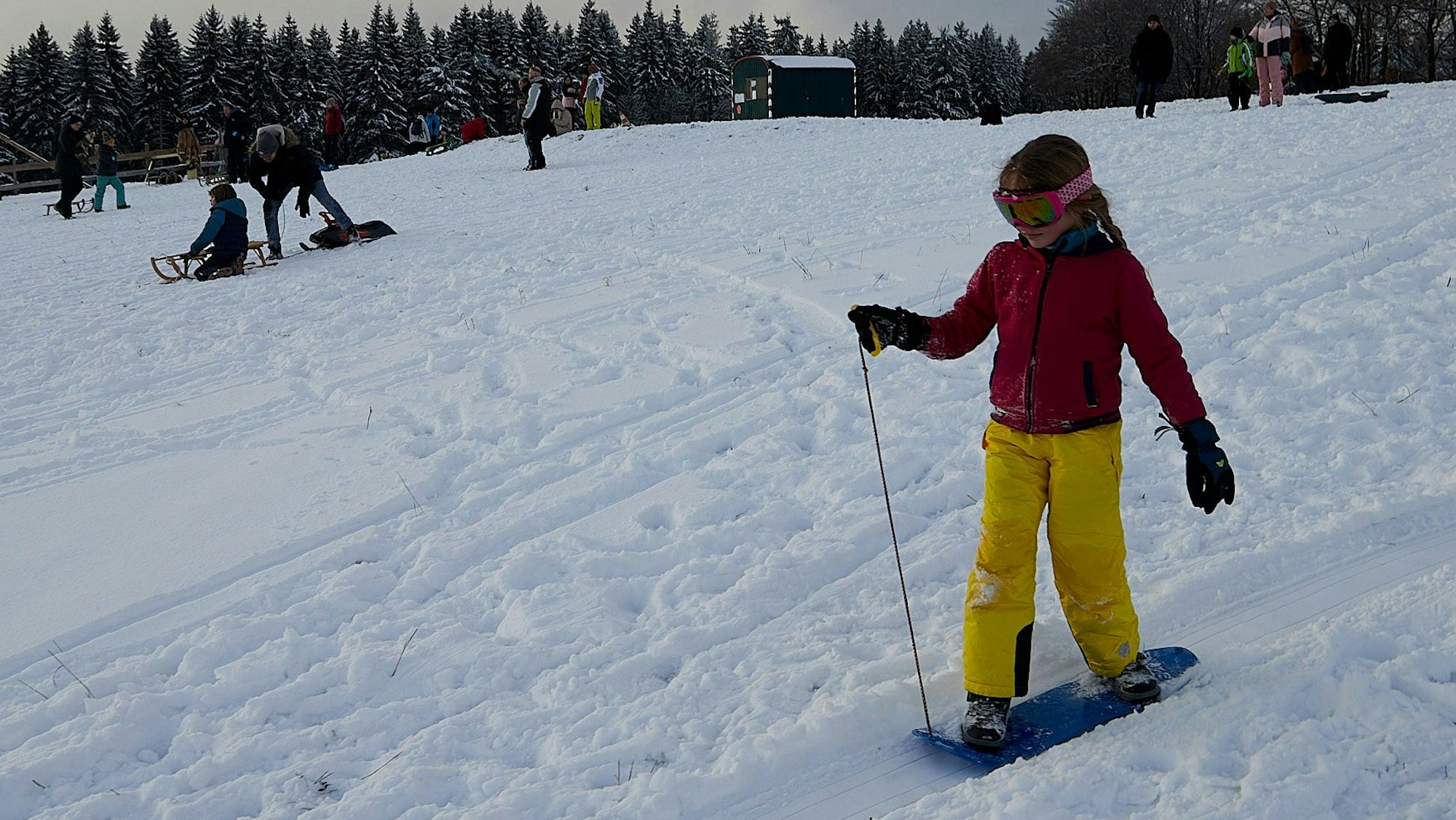 Emma fährt mit dem Snowboard den Hang hinab.