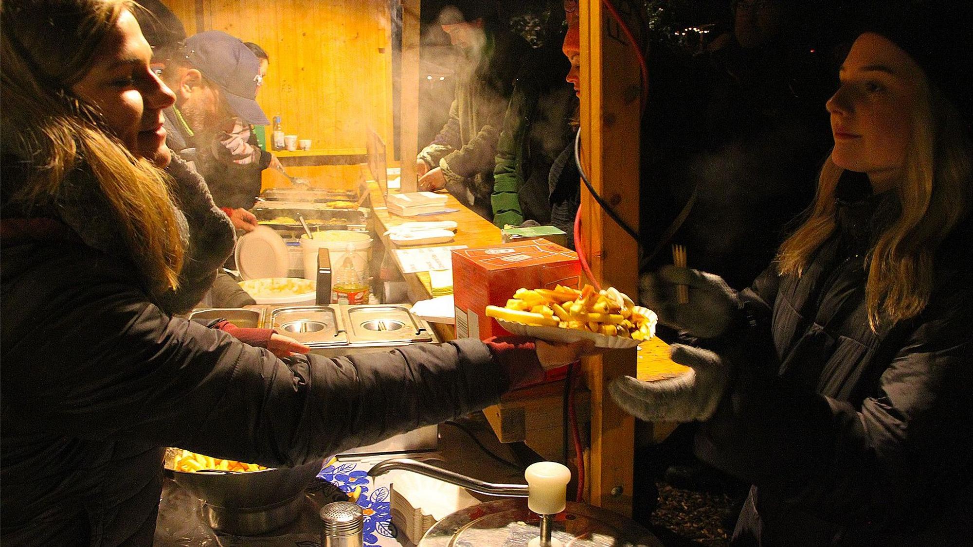 Lea Wiegmann reicht eine Portion Pommes aus der Hütte heraus an eine Besucherin.