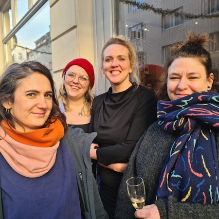 Vier Frauen stehen vor einer Ladenfront. Alles vier lachen selbstbewusst in die Kamera.