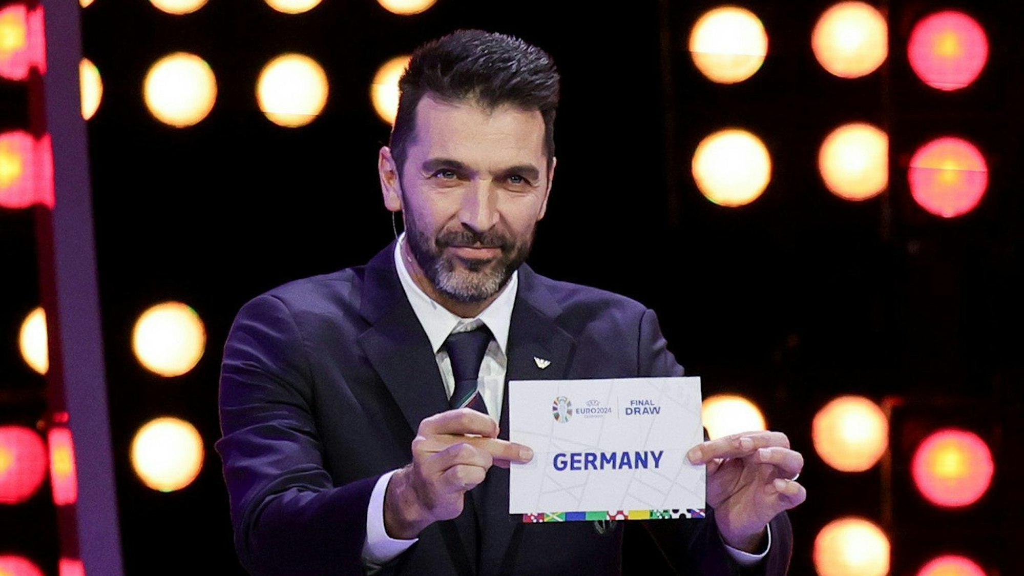 Der italienische Fußballtorwart und Weltmeister Gianluigi Buffon hält bei der Auslosung zur Fußball-Europameisterschaft 2024 einen Zettel hoch, auf dem Deutschland steht.