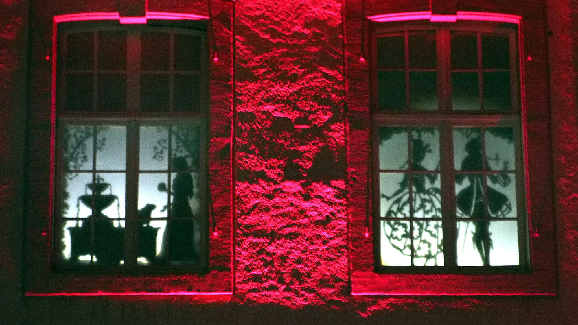 In den Fenstern rot angestrahlten Schlosses sieht man Schattenrisse höfischer Szenen