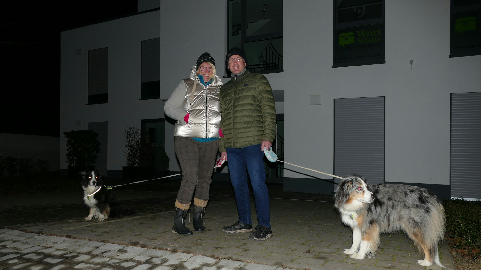 Ein Mann und eine Frau sind mit ihren Hunden in der Dunkelheit unterwegs.