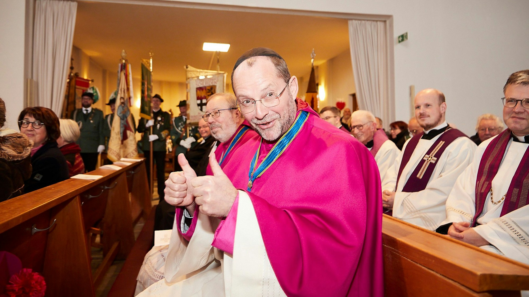 Generalvikar Andreas Frings sitzt in einer Kirchenbank und hält beide Daumen in die Höhe aus Zeichen der Gratulation für den neuen Pfarrer der GdG Schleiden-Hellenthal.