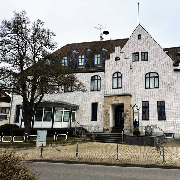 Das Bild zeigt ein großes und weiß verklinkertes Gebäude mit Reliefs rechts und links des Eingangs, auf denen ein Mann und eine Frau zu sehen sind.