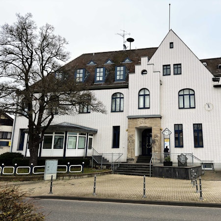 Das Bild zeigt ein großes und weiß verklinkertes Gebäude mit Reliefs rechts und links des Eingangs, auf denen ein Mann und eine Frau zu sehen sind.