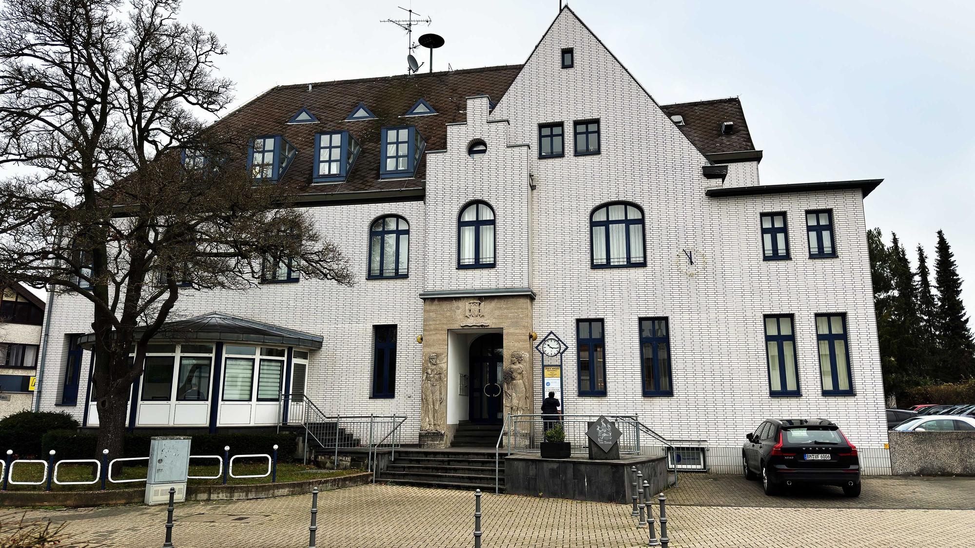 Das Bild zeigt ein großes und weiß verklinkertes Gebäude mit Reliefs rechts und links des Eingangs, auf denen ein Mann und eine Frau zu sehen sind.
