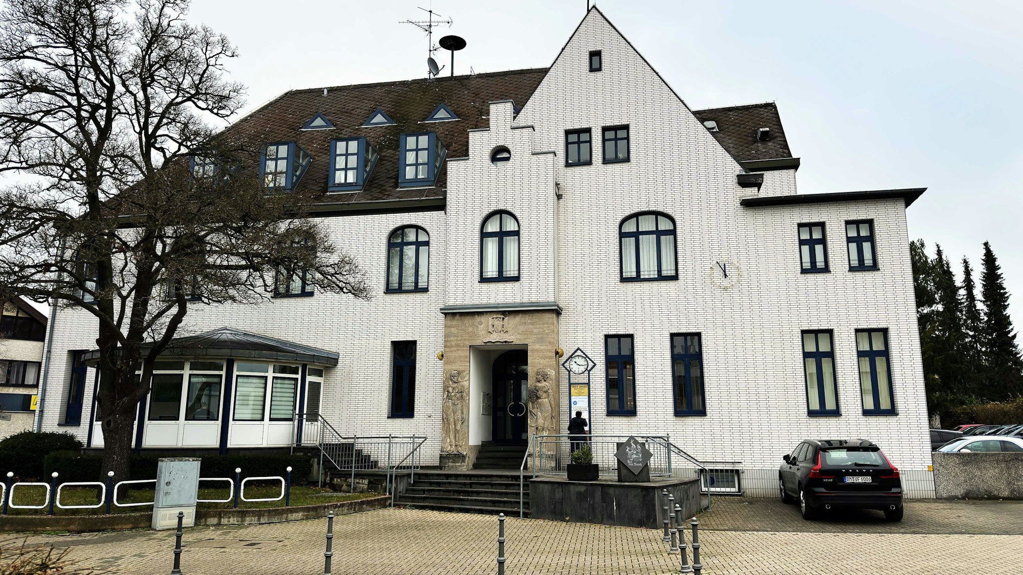 Das Bild zeigt ein großes und weiß verklinkertes Gebäude mit Reliefs rechts und links des Eingangs, auf denen ein Mann und eine Frau zu sehen sind.