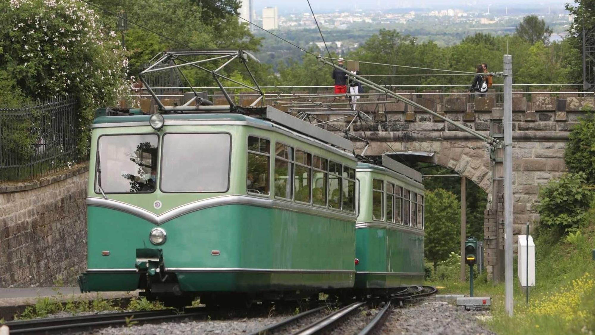Ein grüner Triebwagen fährt in Höhe von Schloss Drachenburg den Drachenfels hinauf.