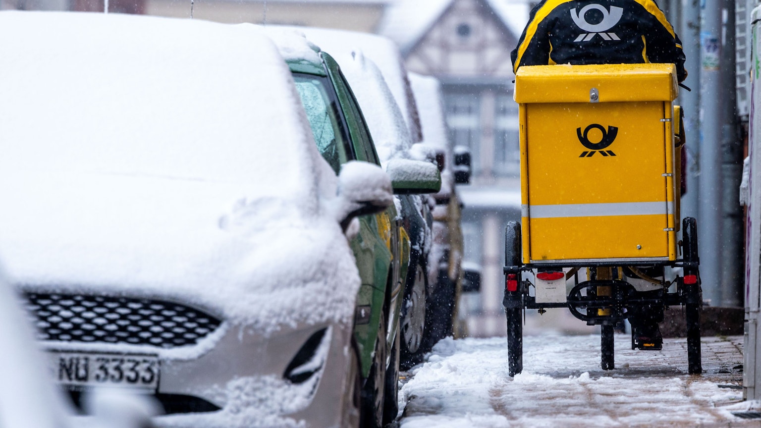 Eine Briefträgerin ist mit ihrem Fahrrad bei starkem Schneefall unterwegs.
